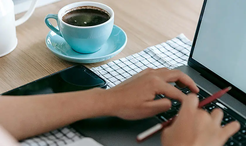 Woman with coffee cup typing on laptop computer.